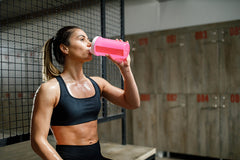 Woman wearing a crop top and leggings drinks a protein shake in the gym
